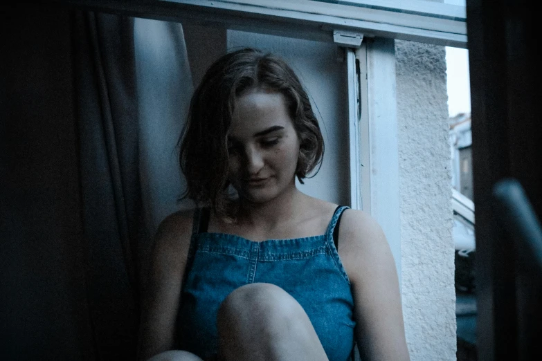 a woman sits alone in the dark in her denim dress