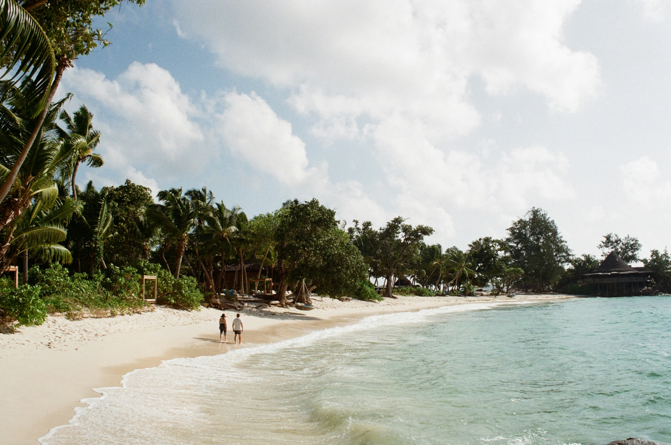 two people walk along the sandy beach near a blue ocean