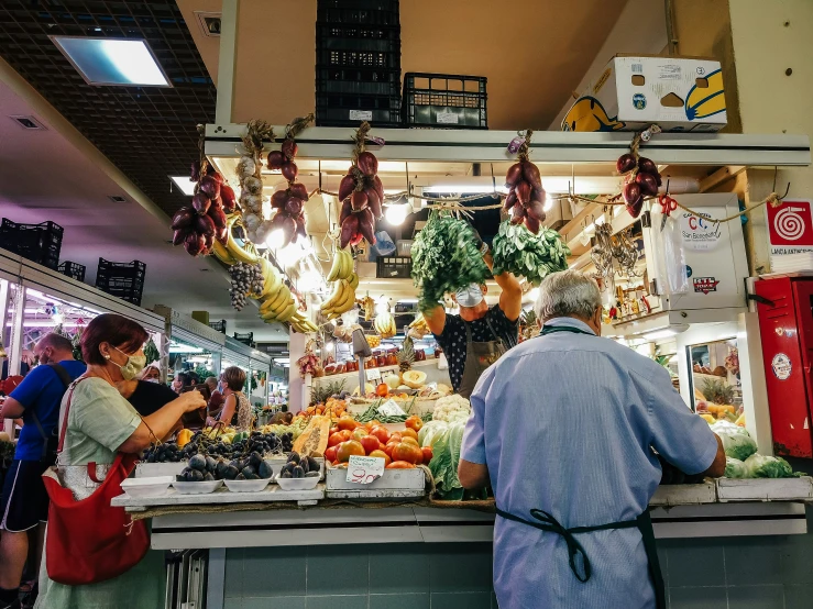 people in a food stand surrounded by lots of vegetables