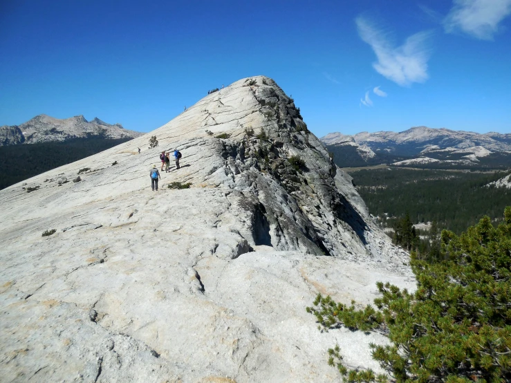 three people on the top of a mountain, two are standing on a mountain peak