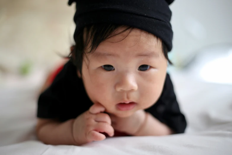 a baby with a black hat lays on top of white sheets