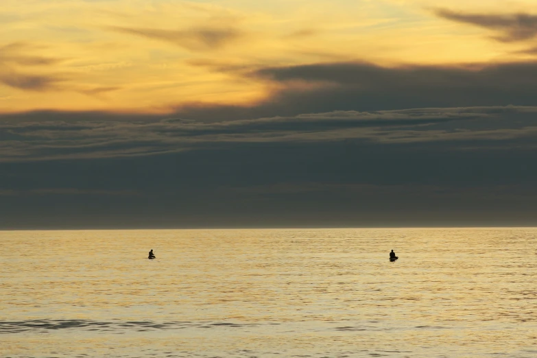 two people on surfboards in the ocean during sunset