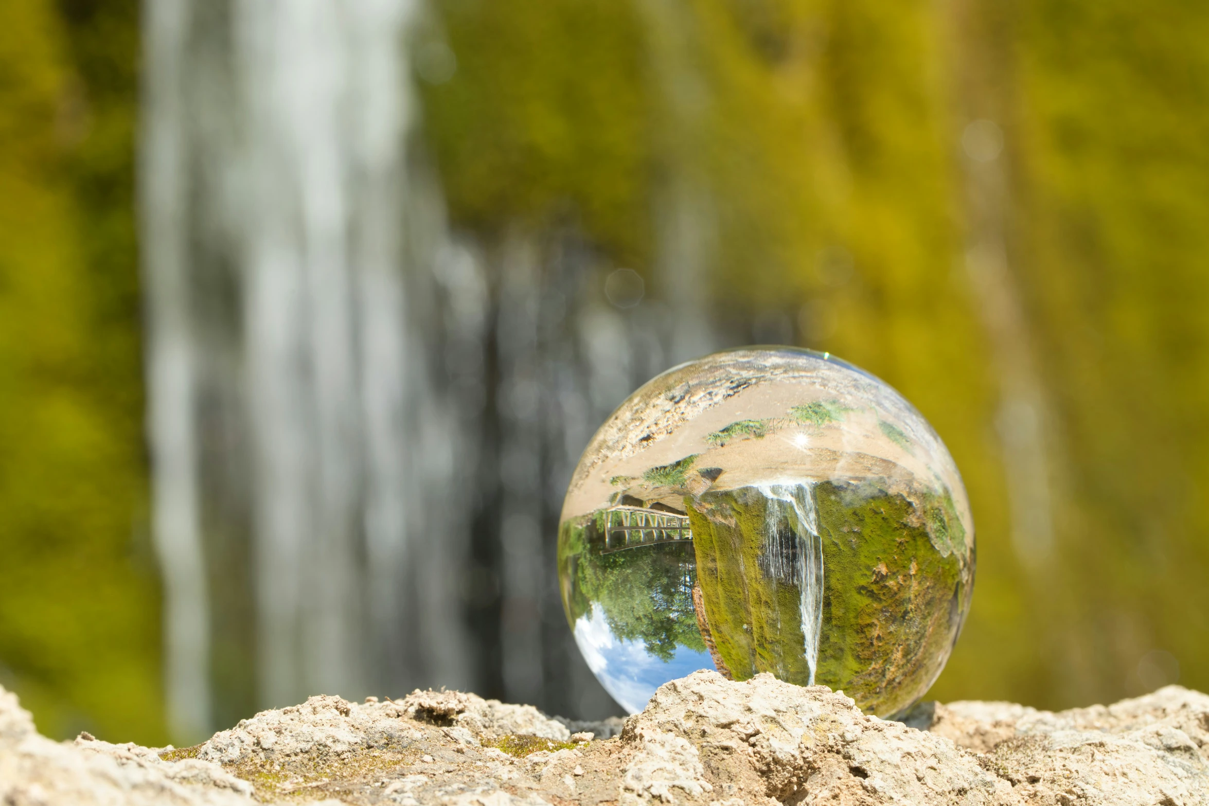 a glass ball sitting on a rock in front of a waterfall