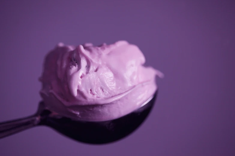 a spoon full of pink ice cream on a purple background