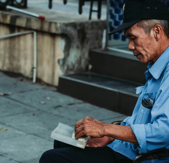 an elderly man reading a book sitting on the sidewalk