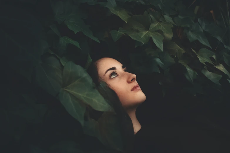 a woman with eyes open sitting down next to leaves