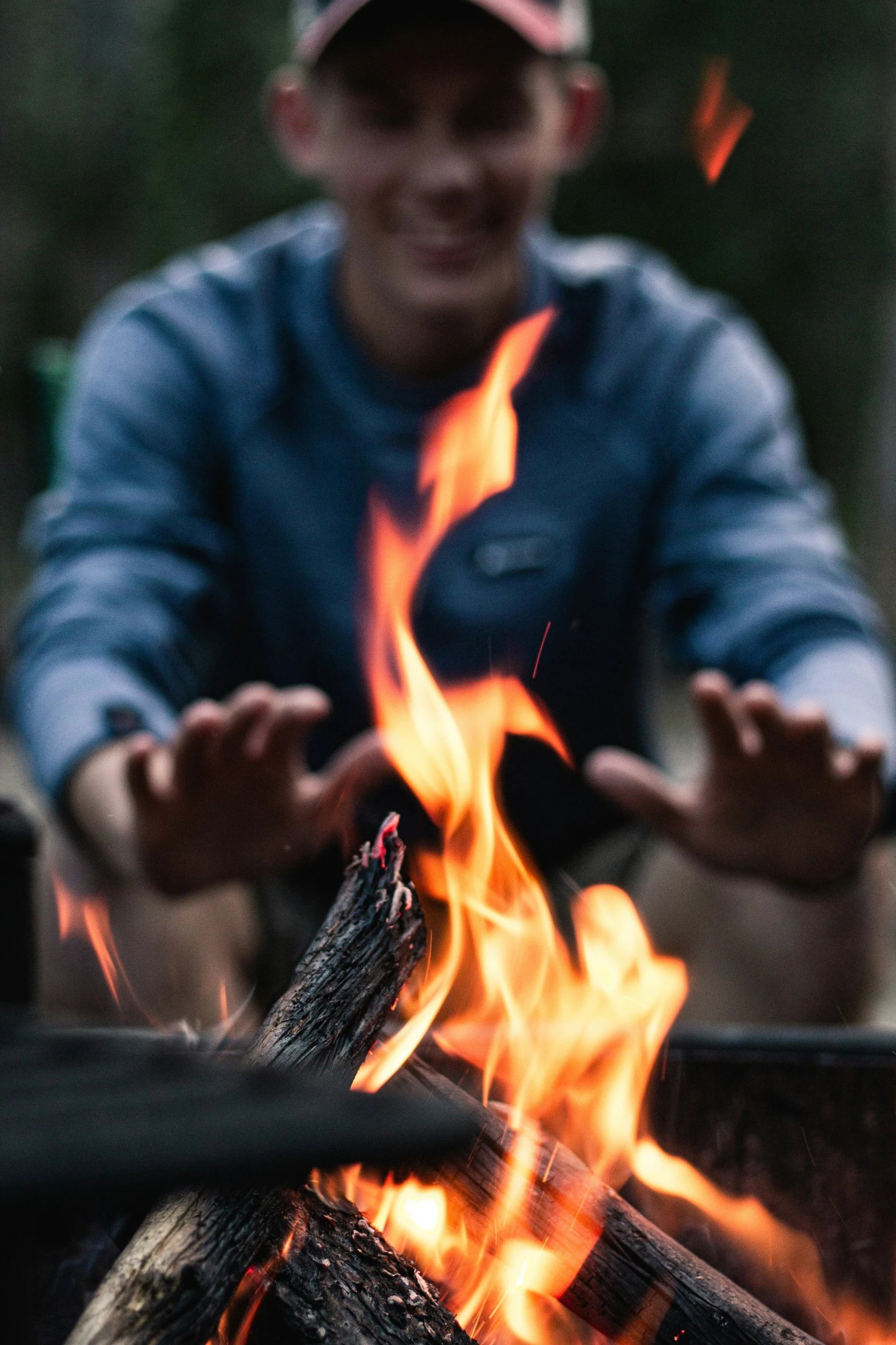 someone sitting near a camp fire with their hands stretched out