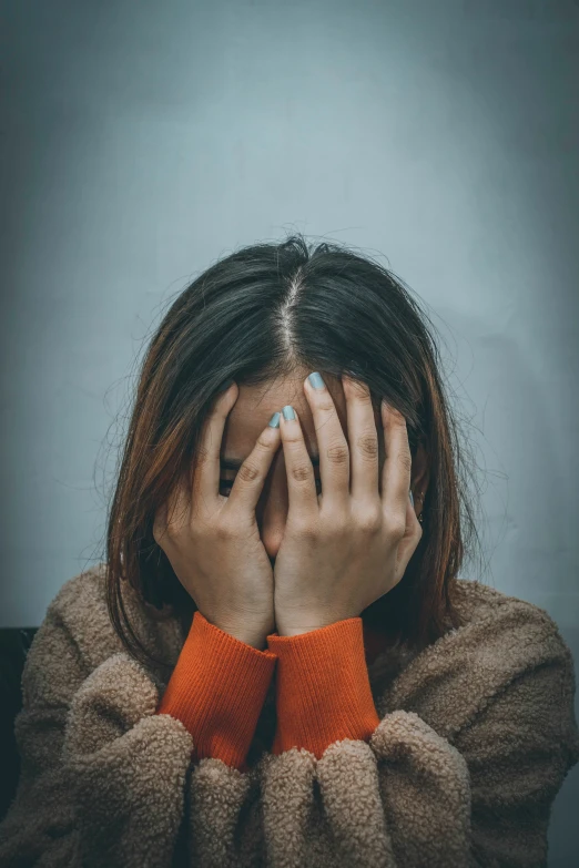 an asian woman covering her face with her hands