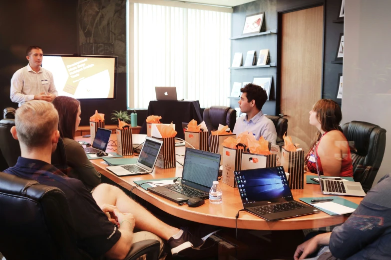 men and women sit in chairs around tables with laptops