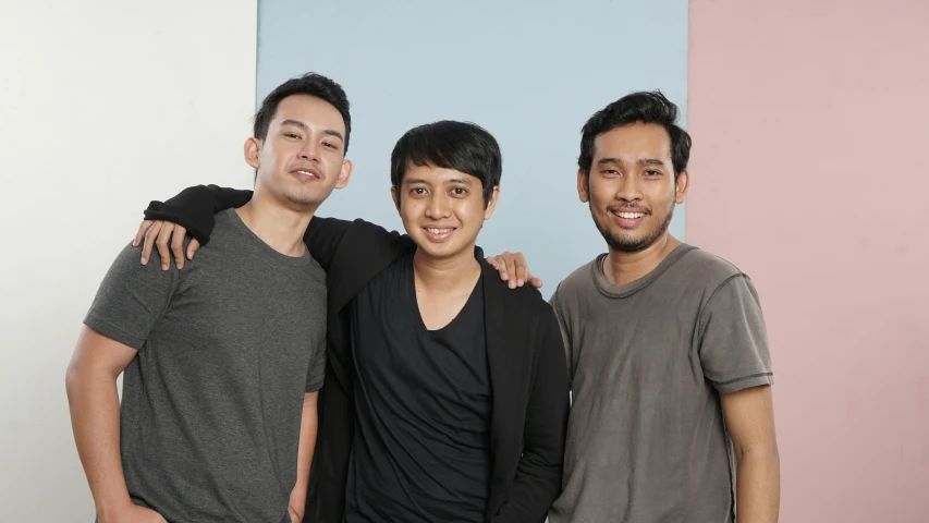 three guys pose in front of a pink wall