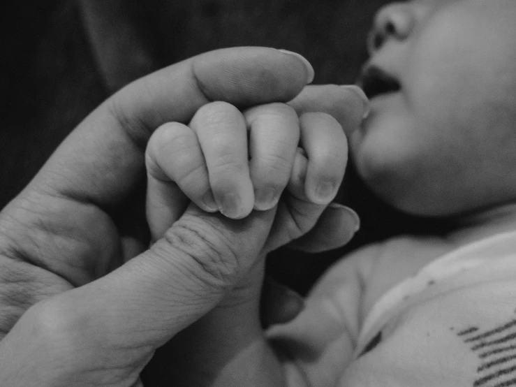 a mother feeds her infant's hand with a bottle of milk