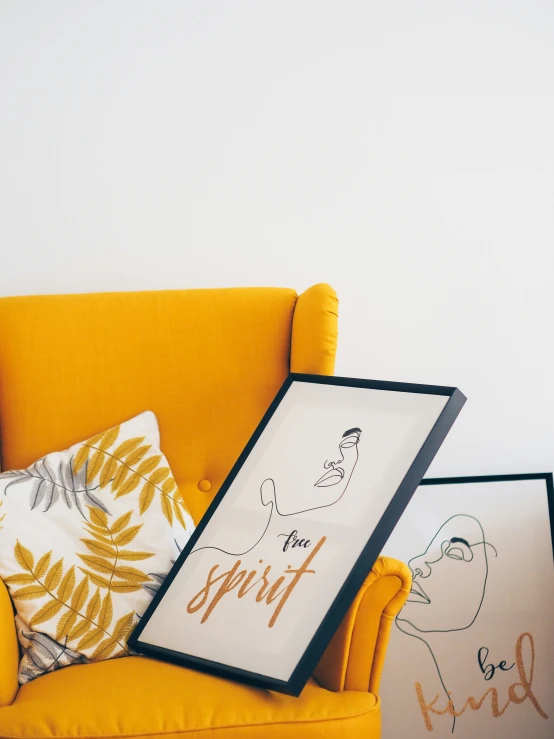 two framed pictures sit on a yellow chair next to some hand drawn art