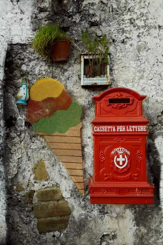 a red mail box sitting against a stone wall with a sign