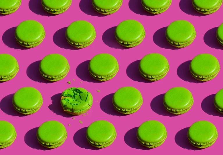 an array of green macaroons on pink background