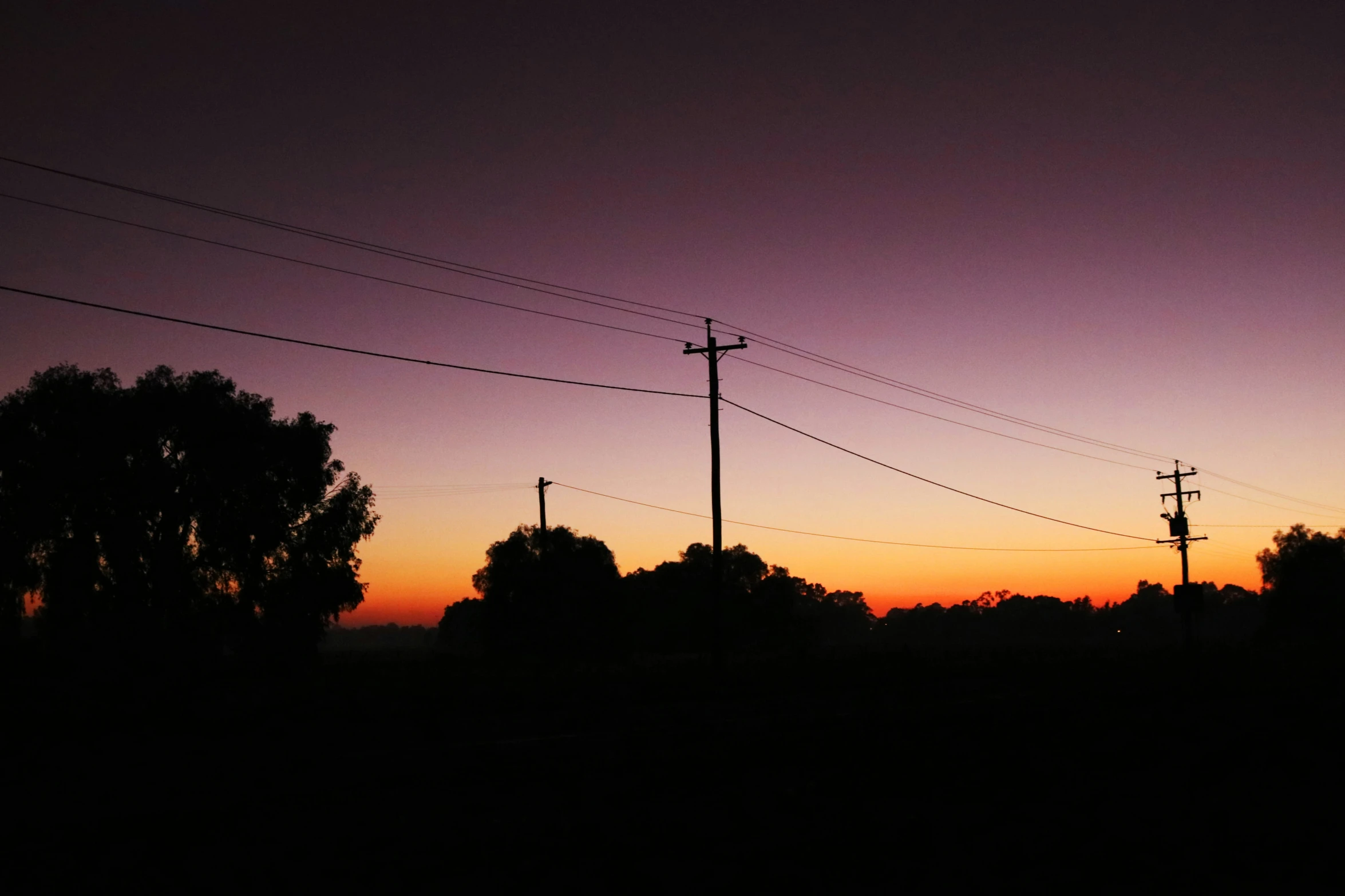 a sunset view of power poles and telephone lines