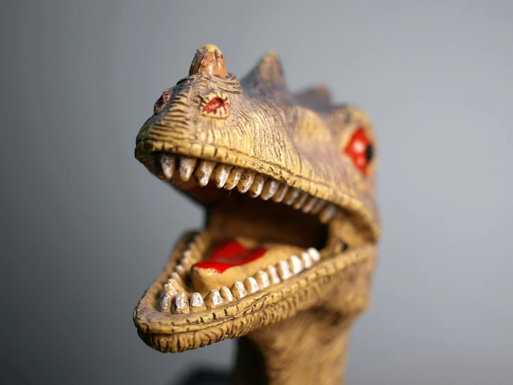 a toy dinosaur with its mouth open with the head slightly down