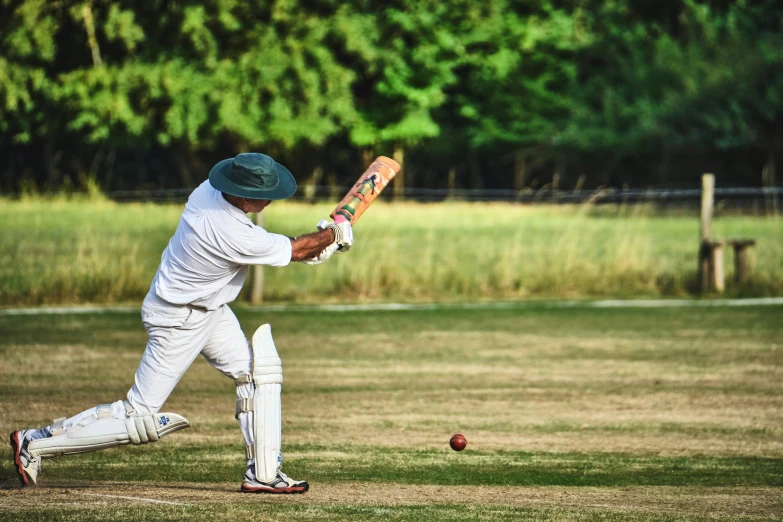 a cricket player holding a bat and ball near his face