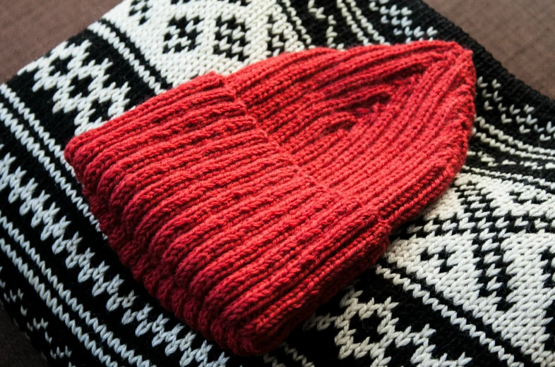 a red hat laying on a black and white knitted blanket