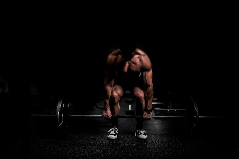 a man squats on top of the barbell in the dark