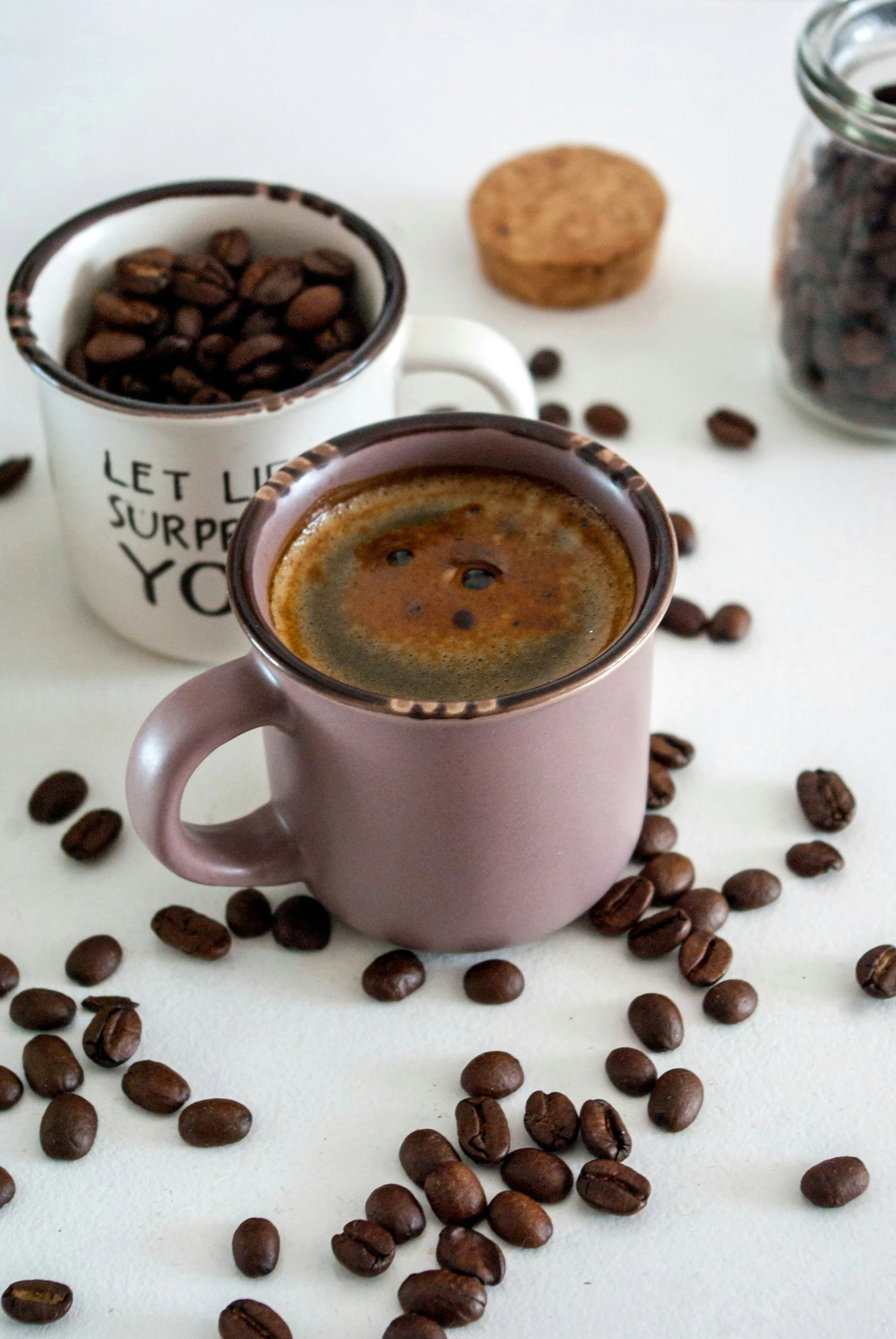 two mugs filled with coffee beans and some cookies