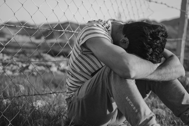 a man is sitting down near a fence with his head to his knees