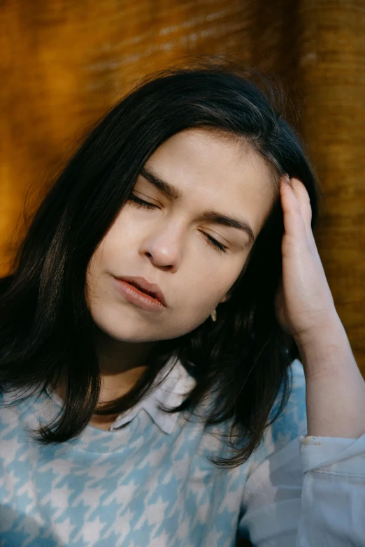 a woman in a blue shirt with long hair holds her hand on her head