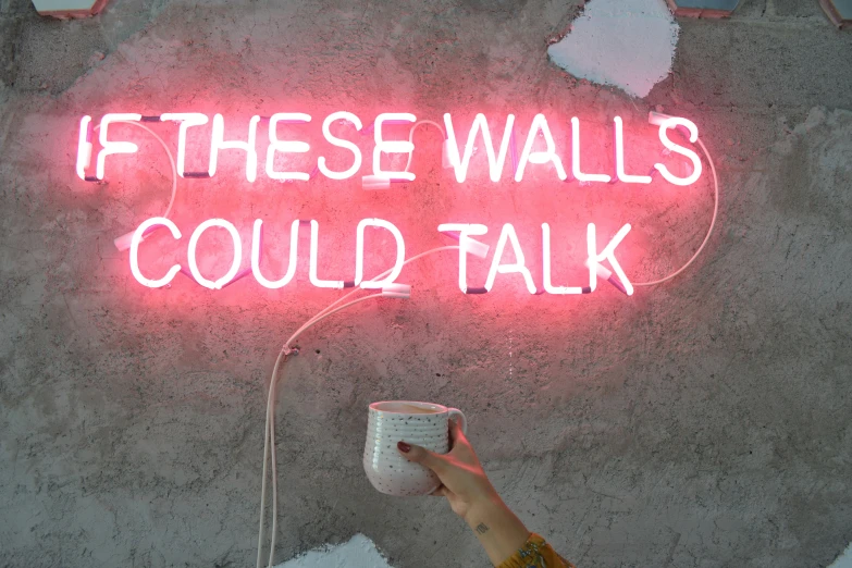 a hand with a cup in front of a neon sign