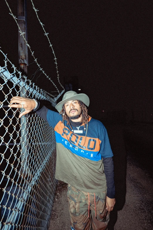 a man wearing an orange and blue baseball cap standing next to a chain link fence