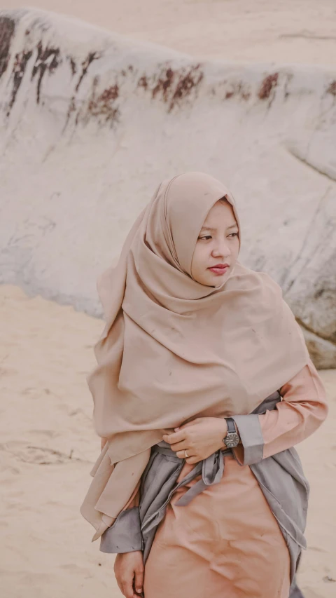 a woman wearing a tan shawl with pink lips standing in the sand