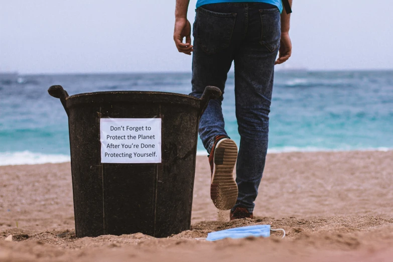 person walking on beach next to a trash can and water
