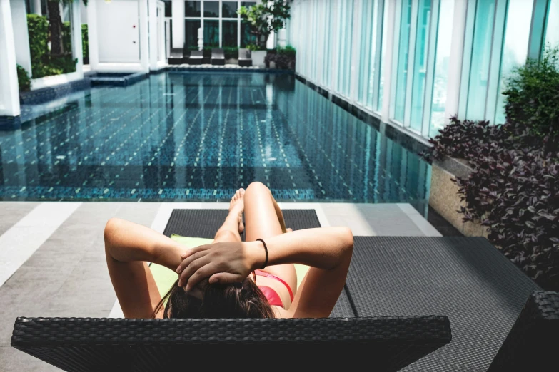 the woman is lounging on the black chair by the pool