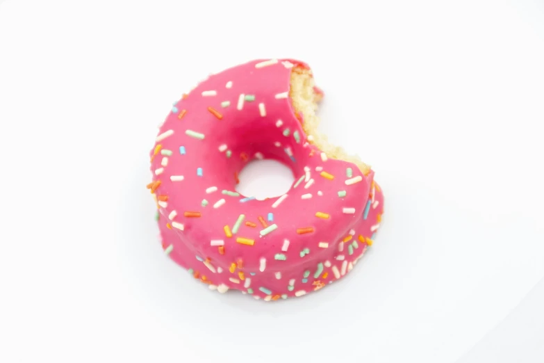 a pink donut covered in sprinkles on a white surface