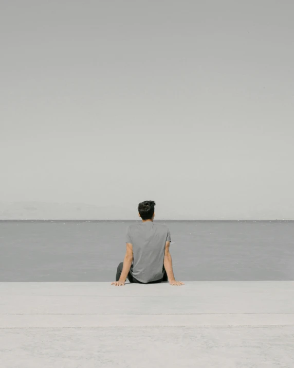 a man sitting on the end of a pier looking at the ocean