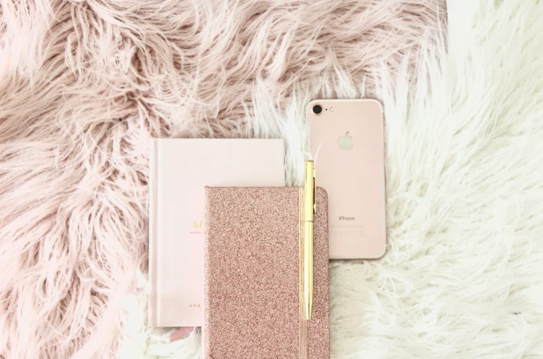 two gold iphones laying next to one another on a fluffy pink background