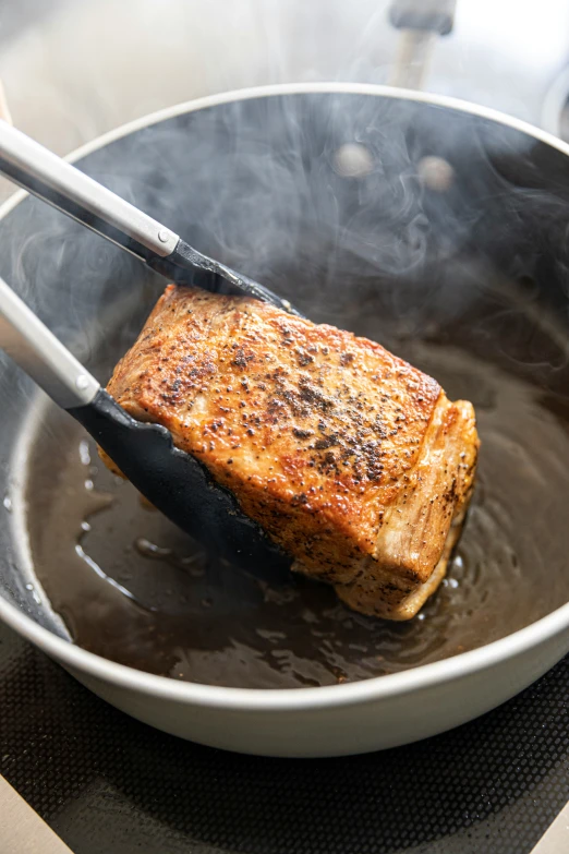 a steak is cooking in a pan with tongs