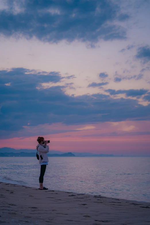 a woman is standing on the beach and flying a kite