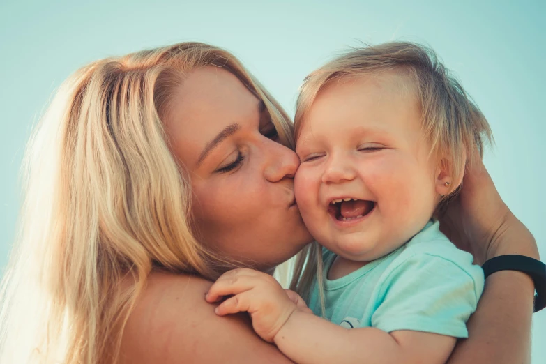 a woman kissing a baby with her head on a girl's shoulders