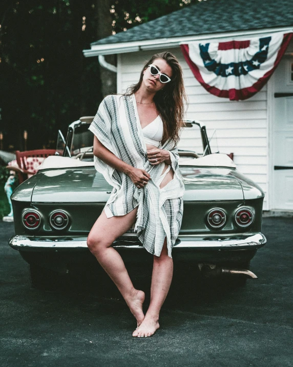 the woman poses in front of a car with her feet on the hood