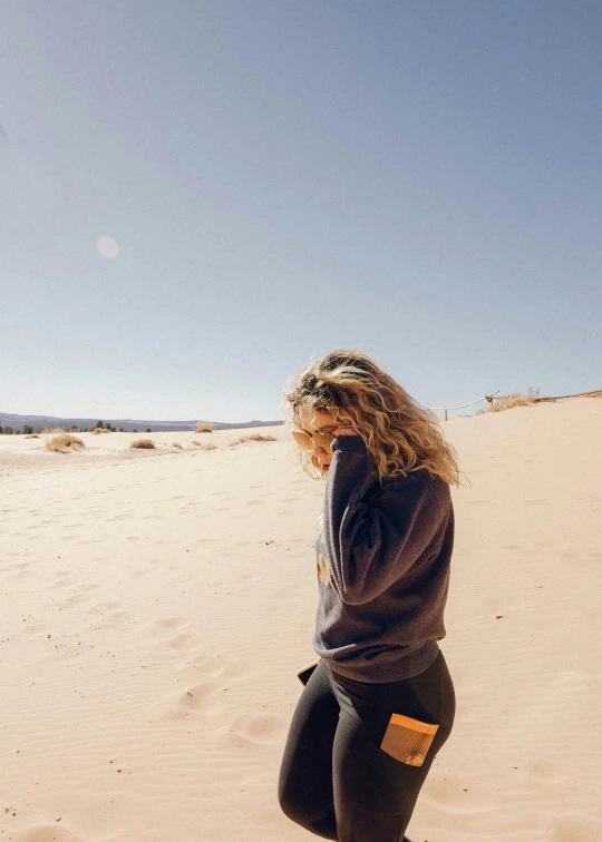 a woman is standing in the sand while she is flying a kite