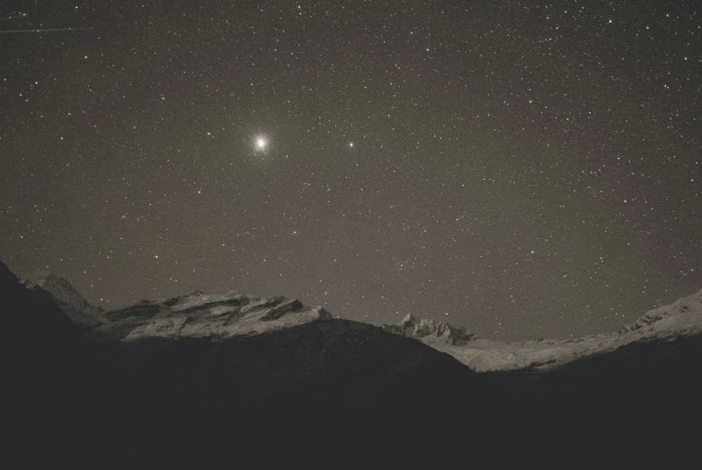 the dark sky above some mountains is filled with stars