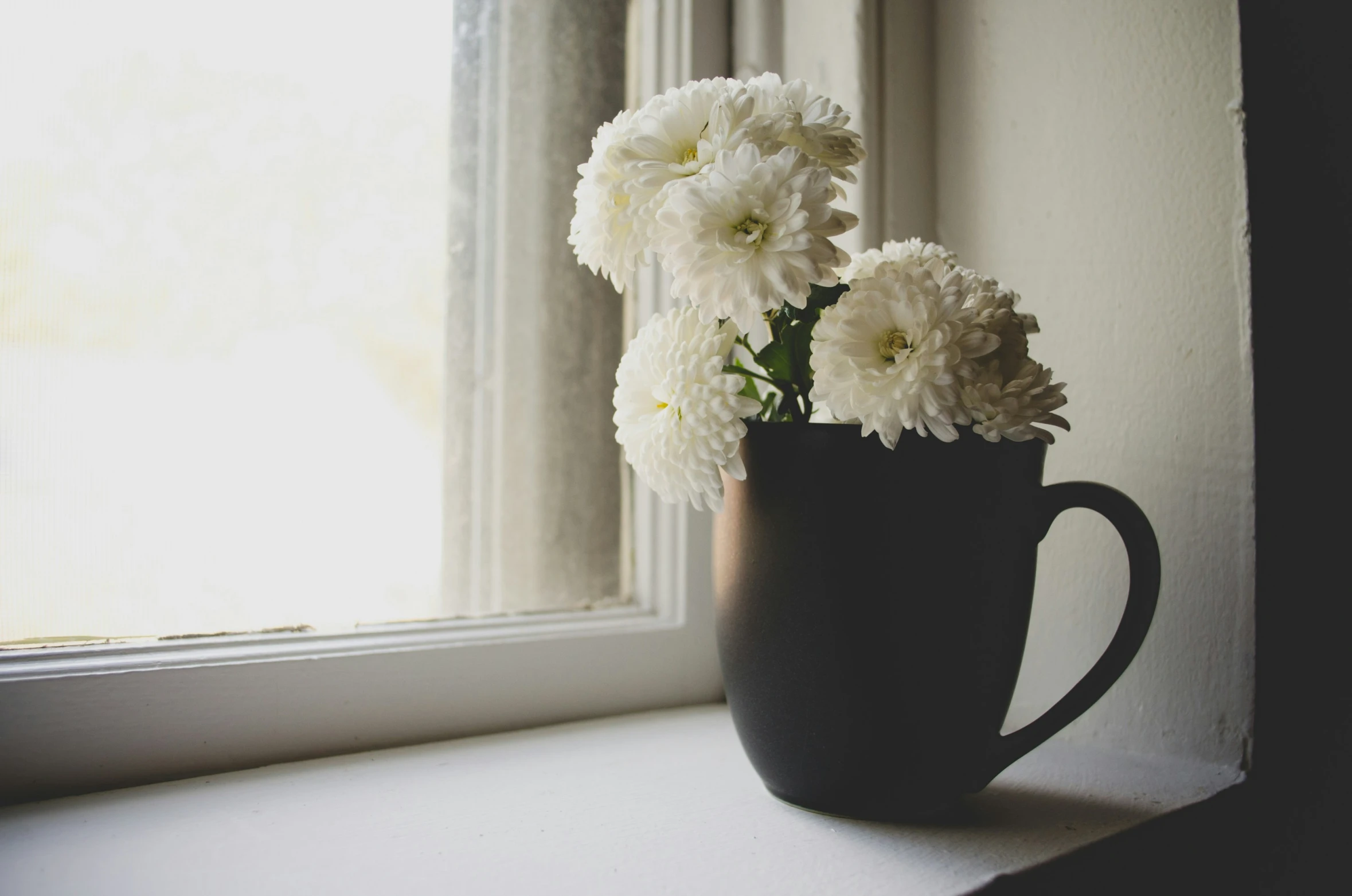 white flowers are placed in a brown coffee mug on the window sill