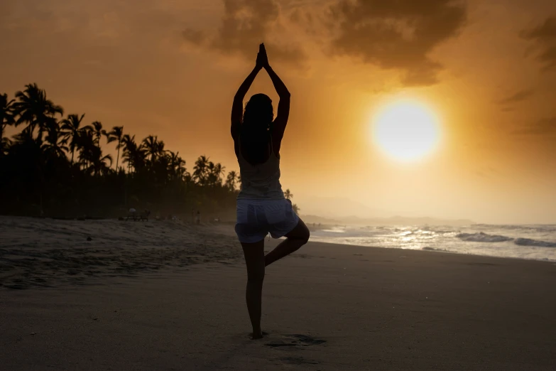 woman practicing yoga on the beach in front of sunset