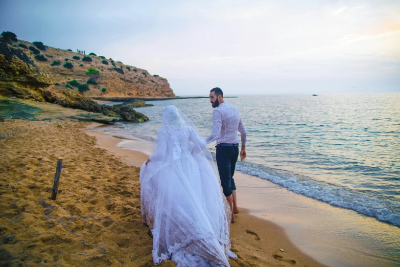 a newly married couple walk along the beach