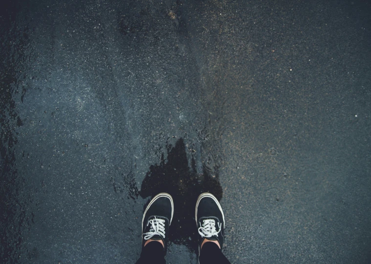 a person wearing sneakers with a wet sidewalk below
