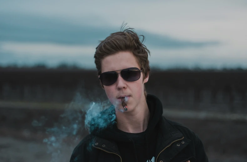 a young man wearing sunglasses smokes a cigarette