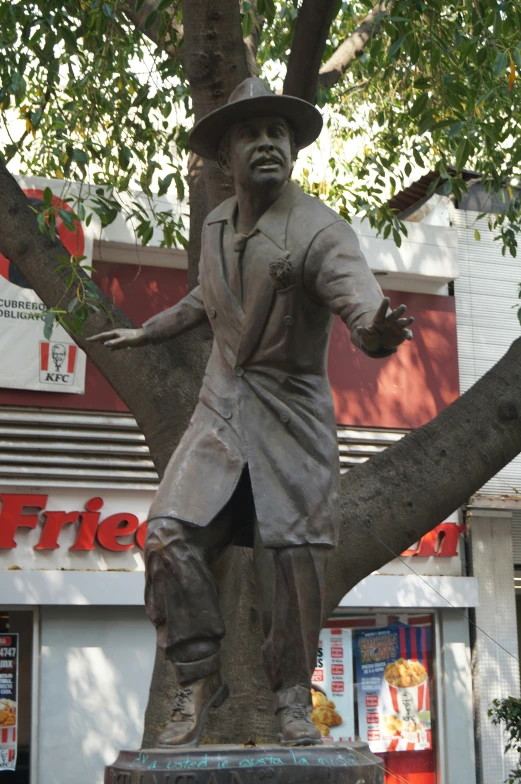 a statue of a man stands on a ledge underneath a tree in front of a store