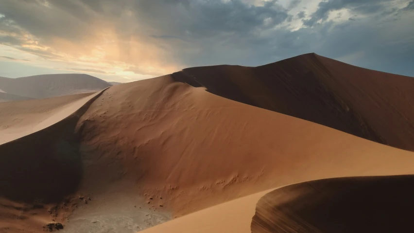 sand dunes and mountains in the distance, with sun peeking out