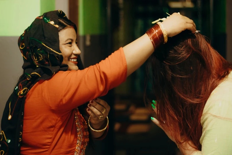 two women in orange shirt with their arms around each other and hair ids