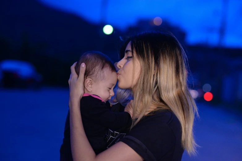 a woman with blond hair holds her baby in a dark lit area