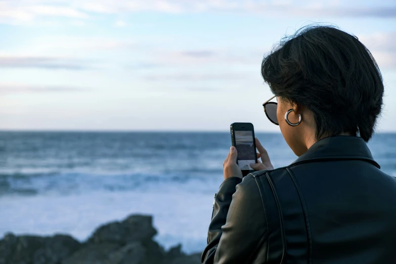 a woman looking at the ocean with her cell phone